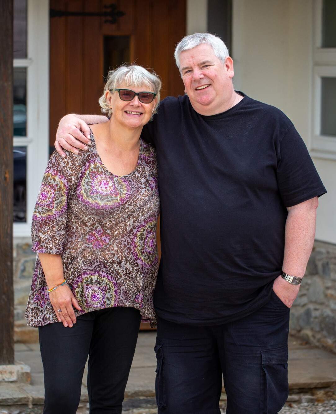 A woman and a man standing outside of their home
