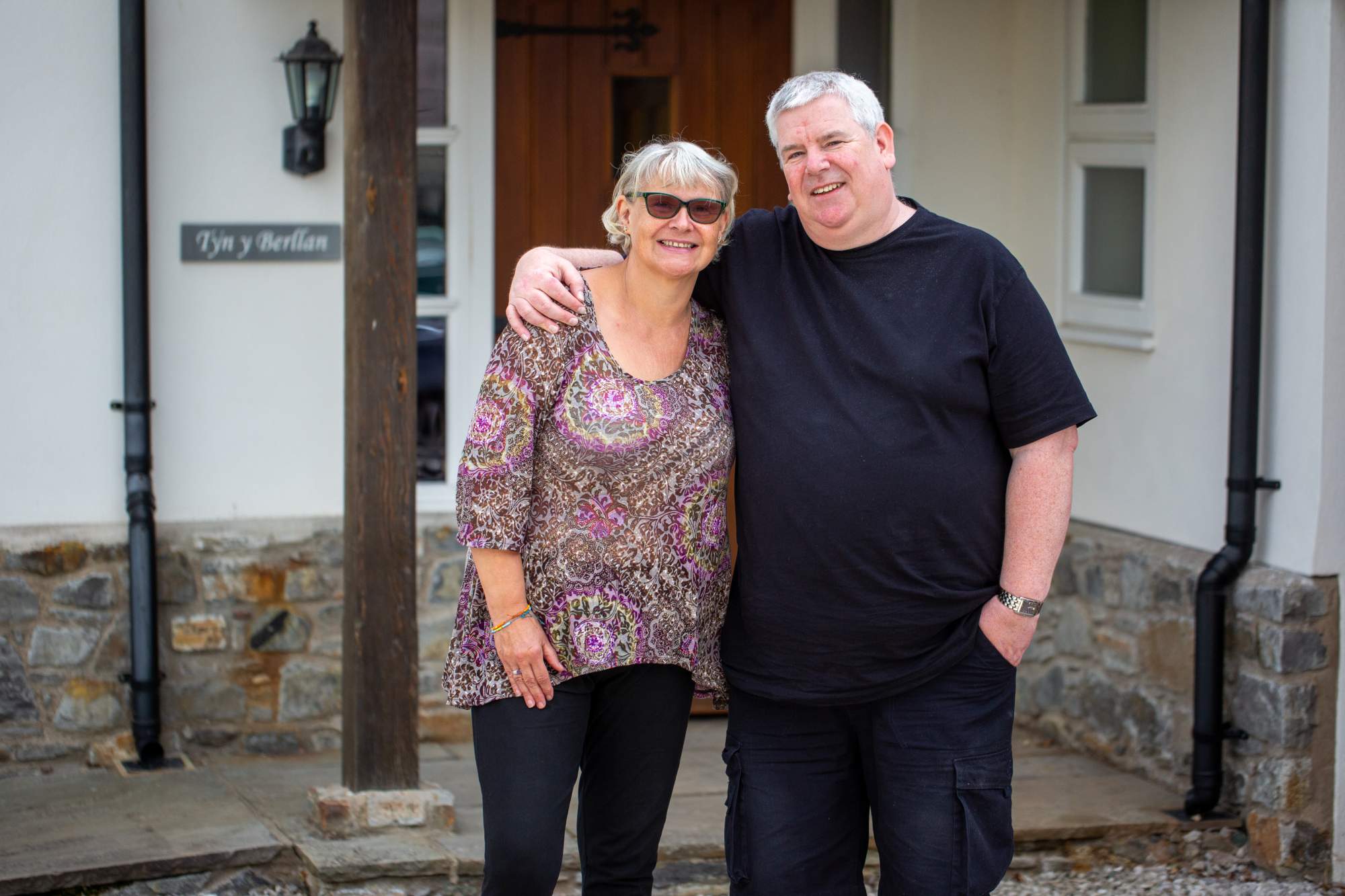 A woman and a man standing outside of their home
