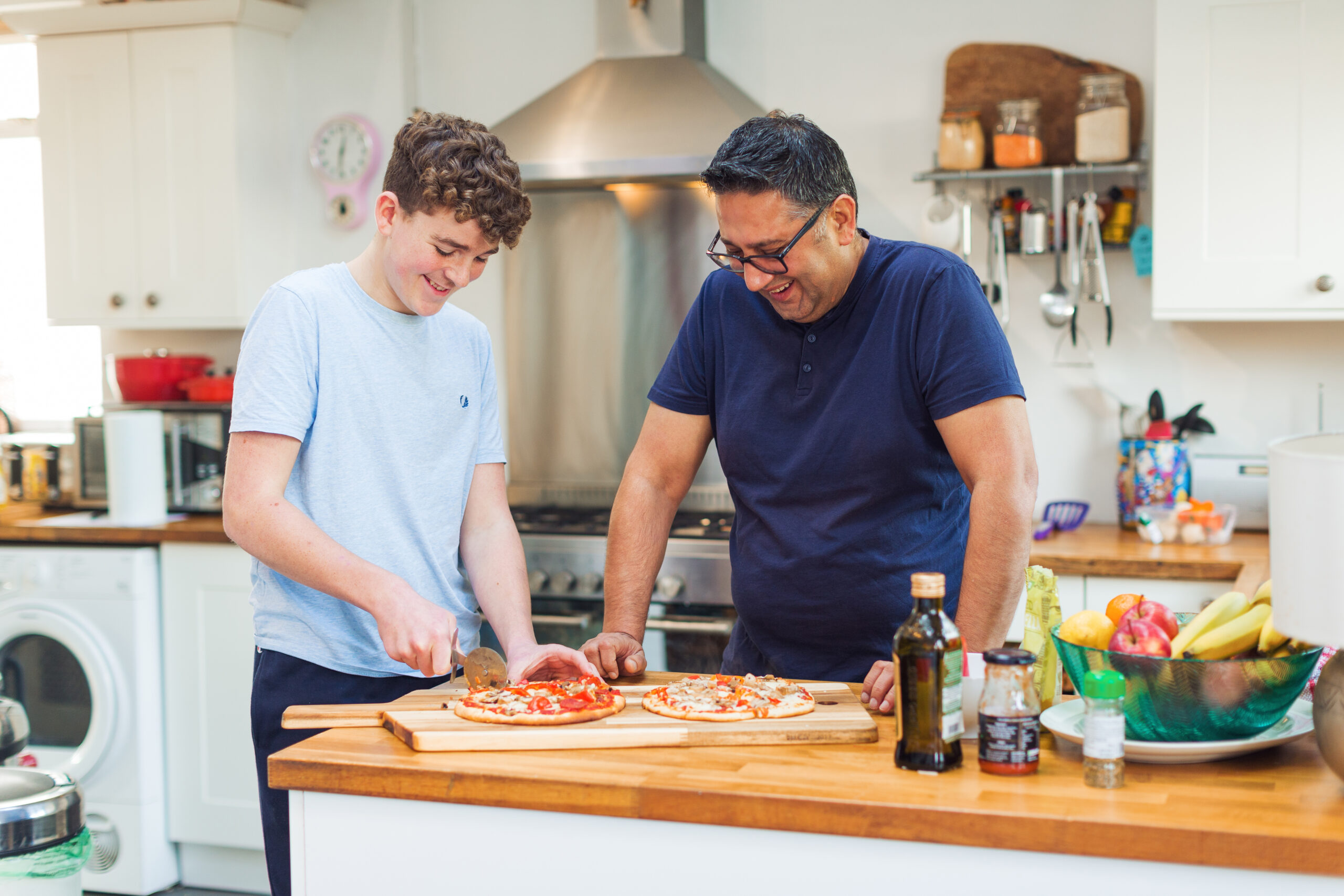 Man and teenage boy cooking pizza in a kitchen