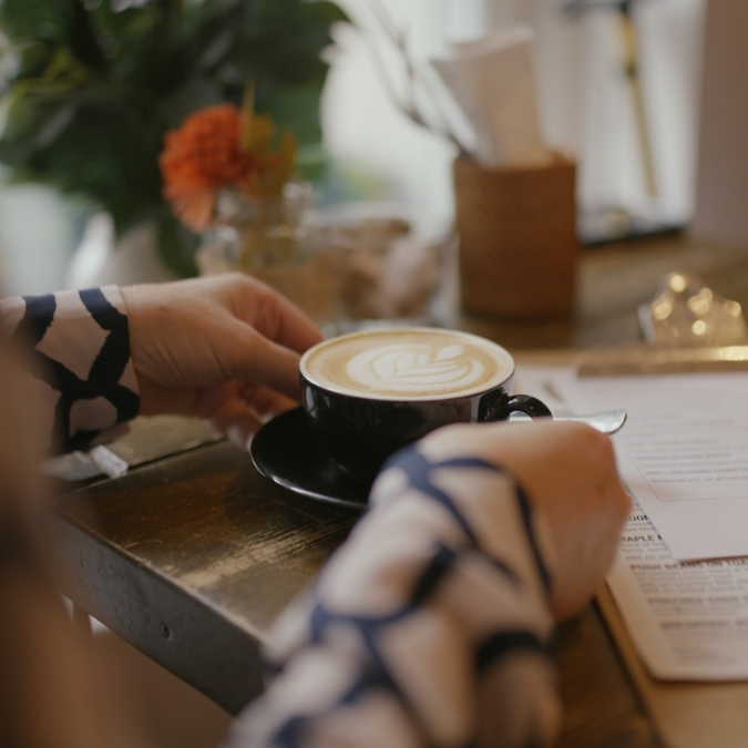 A woman’s hands holding a cup of coffee in a café setting.